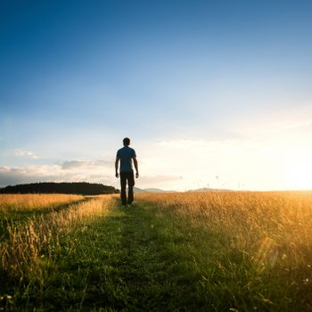 man walking alone through field enjoying nature and the outdoors