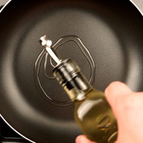 TOP VIEW: Human hands pouring olive oil on the frying pan