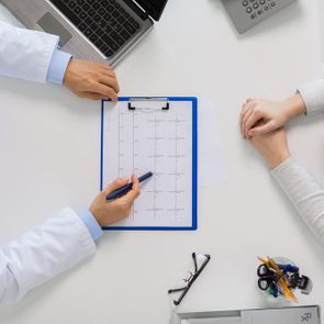 medicine, healthcare, cardiology and people concept - doctor with cardiogram on clipboard and young patient woman meeting at hospital