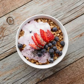 bowl of muesli with yogurt and berries on wooden table, top view