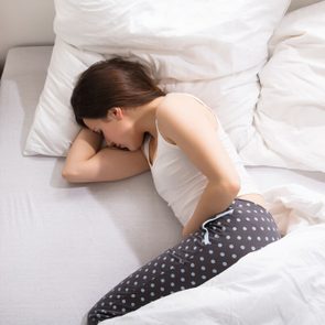 Elevated View Of A Woman Lying On Bed Having Stomach Pain