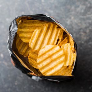 Crinkle cut potato chips on kitchen table. Tasty spicy potato chips in bag. Top view.