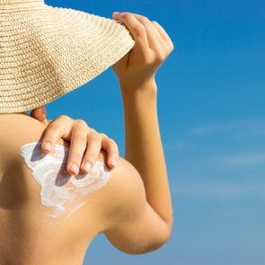 Sunscreen sunblock. Woman in a hat putting solar cream on shoulder outdoors under sunshine on beautiful summer day.