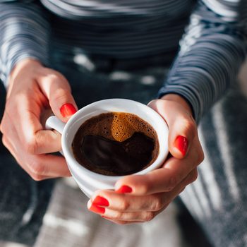 Woman with red nails sitting and holding a hot cup of coffee