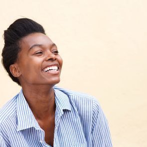 Close up portrait of beautiful young black woman laughing against wall