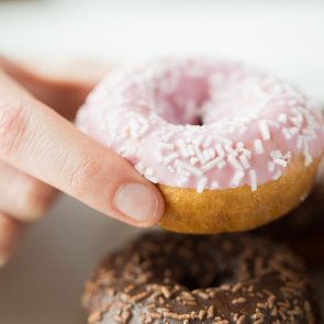 people, food, junk-food and eating concept - close up of female hand holding glazed donut