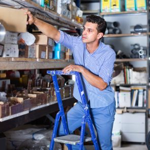 Smiling man in unifom is using ladder to reach the top shelves in the building store.