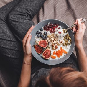 Woman in home clothes eating vegan Rice coconut porridge with figs, berries, nuts. Healthy breakfast ingredients. Clean eating, vegan food concept