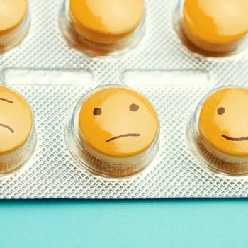 Orange pills and funny faces in a blister on a blue background. The concept of antidepressants and healing