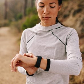 Asian female checking fitness progress on her smart watch. Fit young woman runner checking time on smart watch.