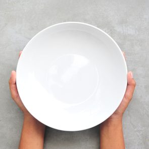 Female hands hold empty dish on stone background.