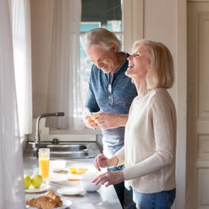 Happy loving senior couple having fun preparing healthy food on breakfast in the kitchen, mature smiling man and woman laughing cooking together on weekend morning, aged old family at home concept