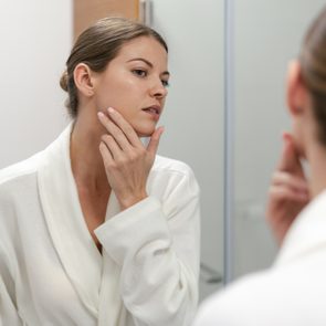 Woman in bathrobe looking in mirror at bathroom