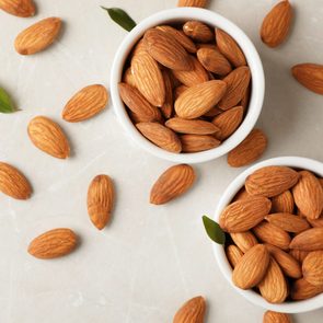 Tasty organic almond nuts in bowls and space for text on table, top view