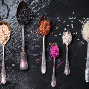 Directly Above Shot Of Various Rice In Spoons On Wet Slate