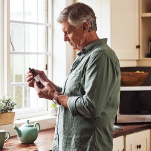 mature man holding bottle of CBD oil in kitchen