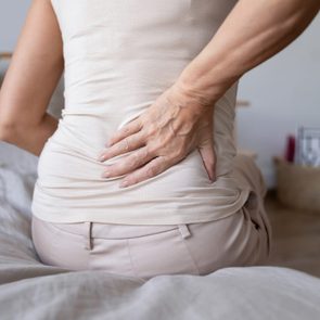 Old mature woman sit on bed touch back feel backpain