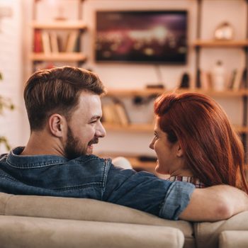 Back view of happy couple talking while watching TV at home.