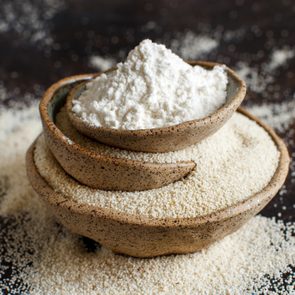 Raw fonio flour and seeds in bowls on dark background