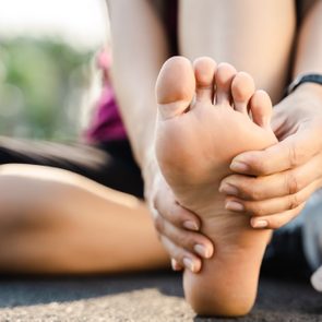 Low Section Of Woman Touching Foot In Pain While Sitting On Road