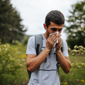 One young man sneezing in blooming nature on sunny spring day