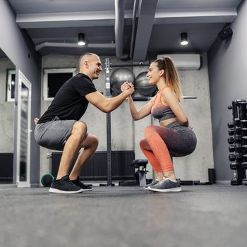 The concept of sports interesting and different fitness training. The couple does sports exercises together. They maintain balance by holding hands and doing squats, couple relationship goal